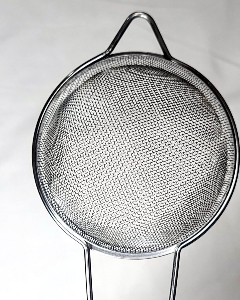 COLAROA fine mesh strainer cup seated in the solid stainless wire frame, showing the spring-fit joint with no weld between handle and cup